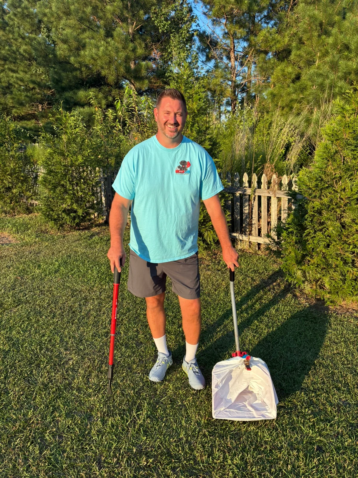 Smiling Scoop Lab team member holding dog waste removal equipment beside a residential gate